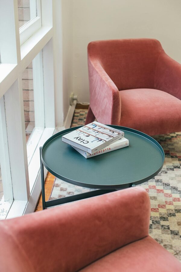 High angle of books placed on small round table near comfortable pink velour armchairs in stylish apartment