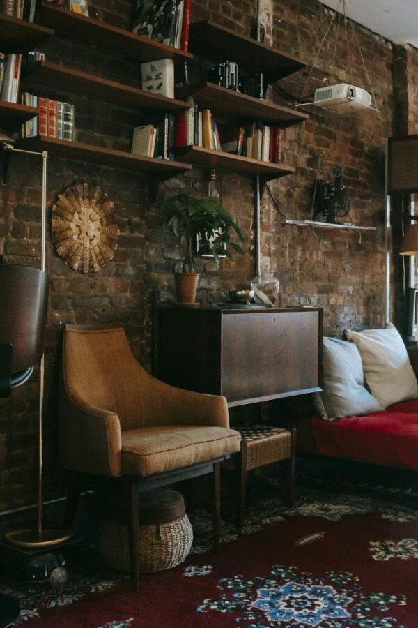 Interior details of cozy apartment with wooden cabinet and comfortable armchair placed near brick wall decorated with bookshelves and potted plant