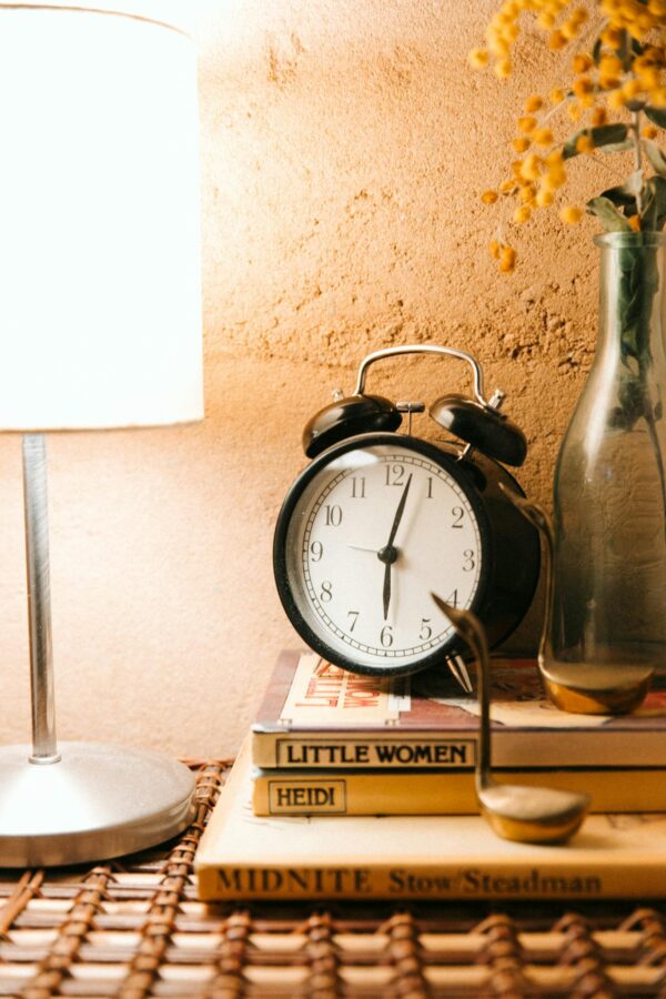 Vintage alarm clock and luminous lamp placed on bedside table